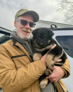 Rescued Rollers Director, John Lizotte holds Chance, the German Shepherd puppy with PRAA